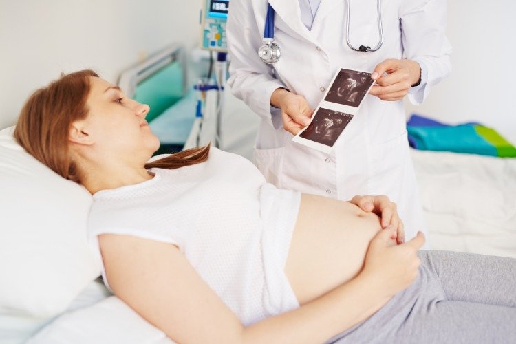 läkare visar bild av foster på sjukhus till gravid kvinna i sängen