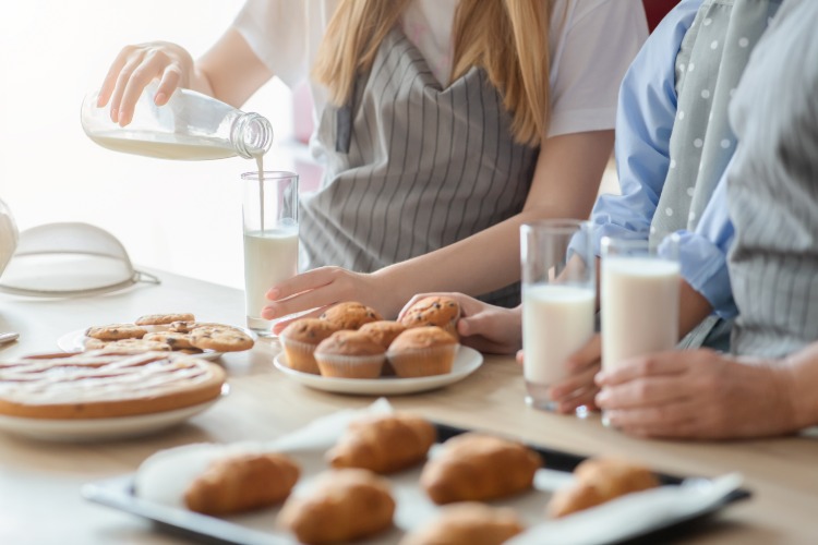 kvinna häller mjölk i glas med bakverk på ett bord