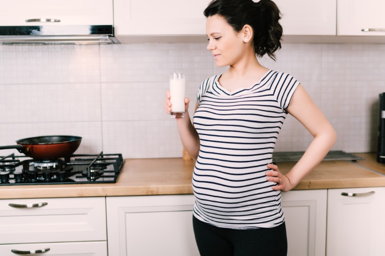 gravid kvinna som håller glas mjölk i köket
