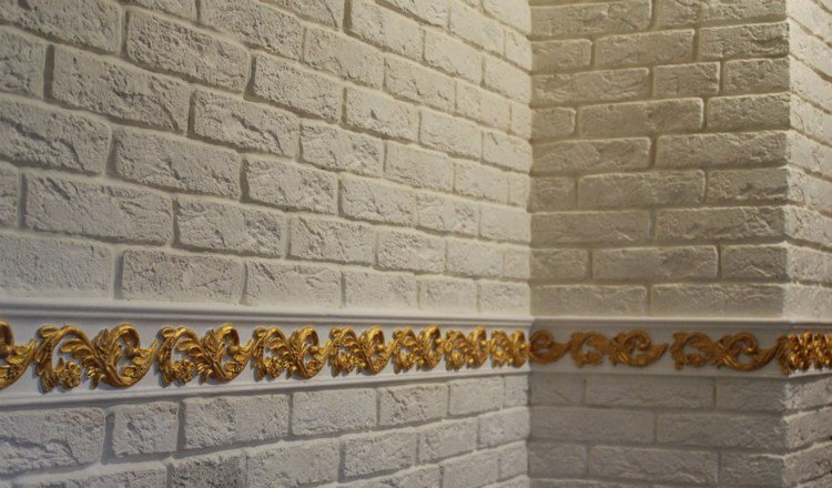 stuckaturgjutning-gips-guld-målning-vägg-dekoration-mot-tegel