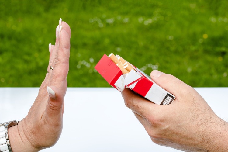 Kvinnlig arm gör en ihållande gest mot paket cigaretter utomhus