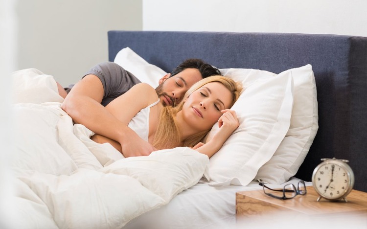 man och kvinna sover tillsammans i sängen med väckarklocka och glasögon på sängbordet