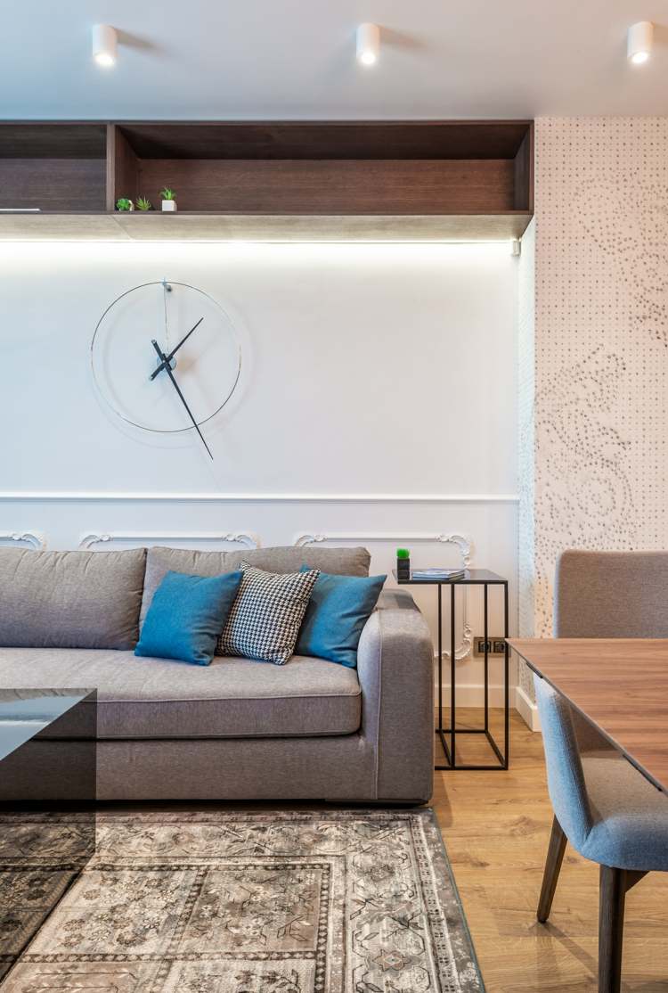 Vardagsrum i modern och tidlös stil med en grå soffa och en original klocka som väggdekoration