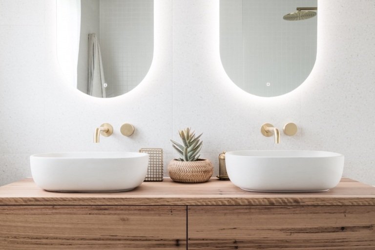Moderna badrum med handfat i trä och bänkskåp och badrumsinredning i guldoptik och speglar med belysning och vita granitplattor