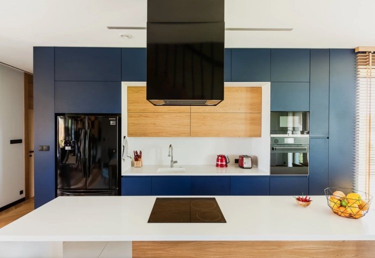 modernt kök med blå fronter och träväggar, vit bänkskiva och bakvägg som kontrast