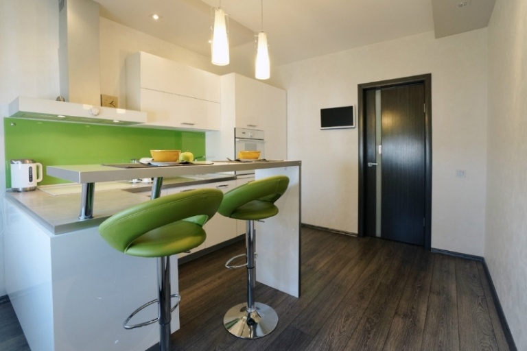 modernt-litet-kök-vit-halvö-disk-grön-stänkskydd-barstol-trägolv