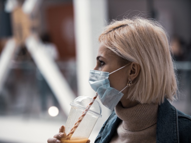 kvinna med skyddsmask dricker juice från ett sugrör under covid 19 -pandemin