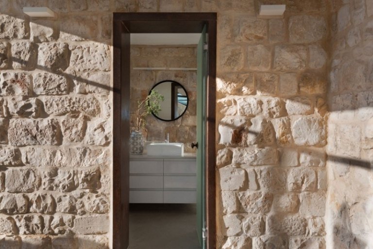 Naturstenmur-inuti-utsida-murverk-dörr-rund-spegel-diskbänk-vit-bänkskåpslådor