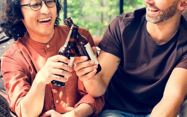 två leende vänner som dricker öl som stöter på ölflaskor