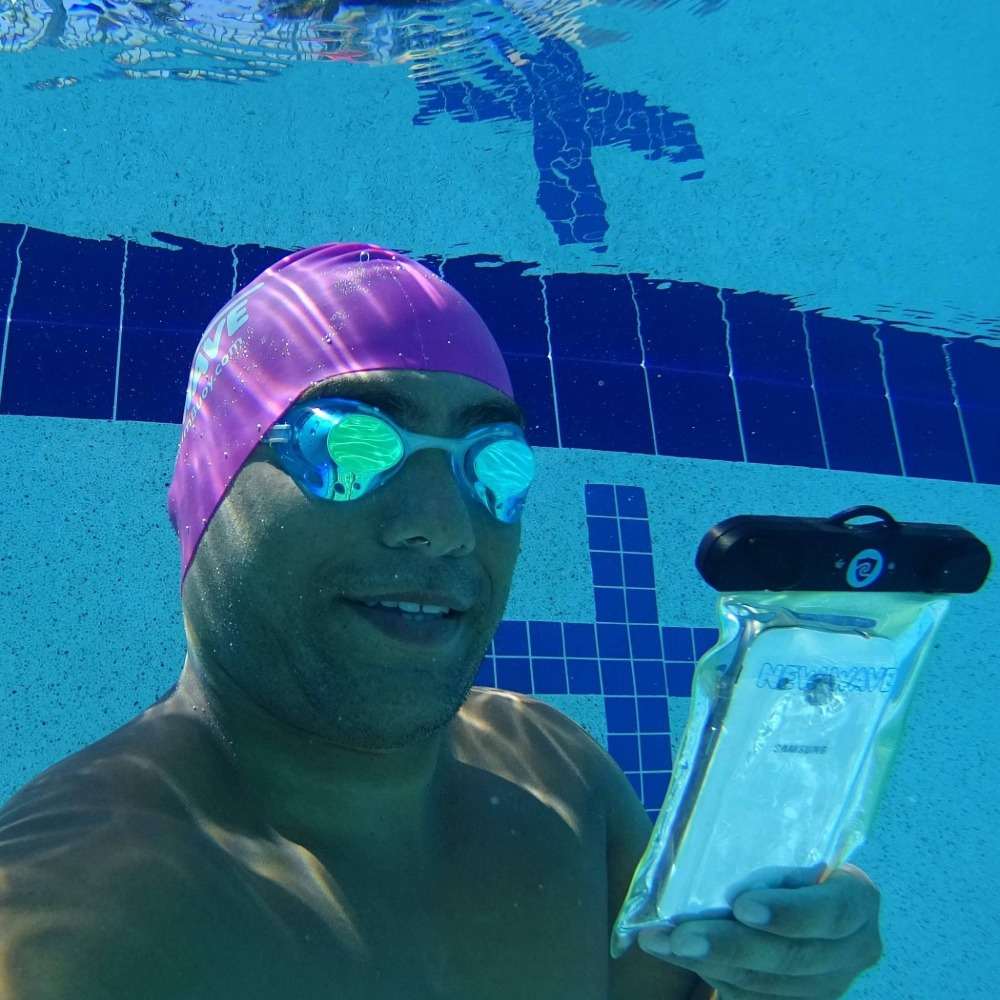 man i poolen med vattentätt telefonväska och dykmask tar en bild under vattnet