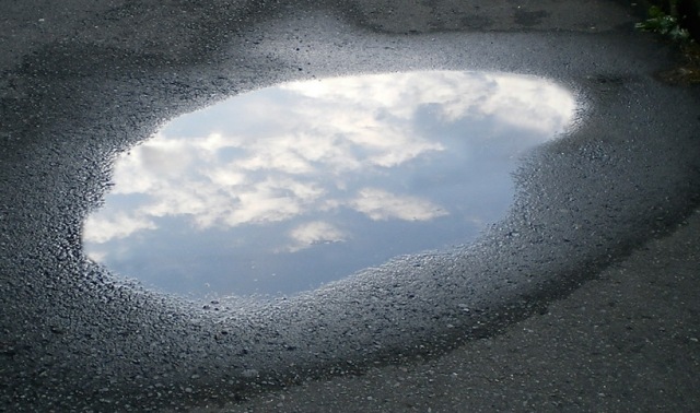 Vattenpöl i asfalt reflekterar himlen