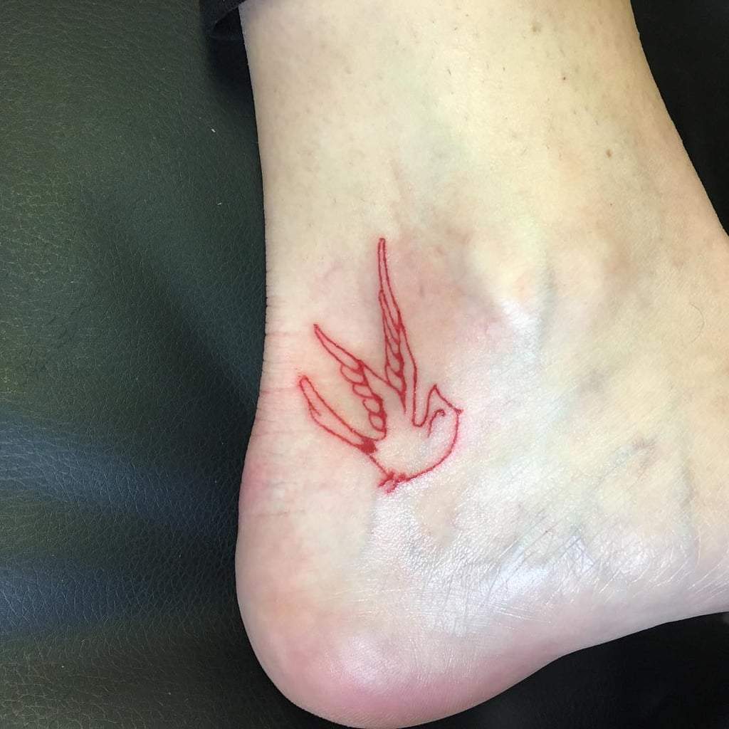 Liten fågel på foten i röd tatueringsfärg