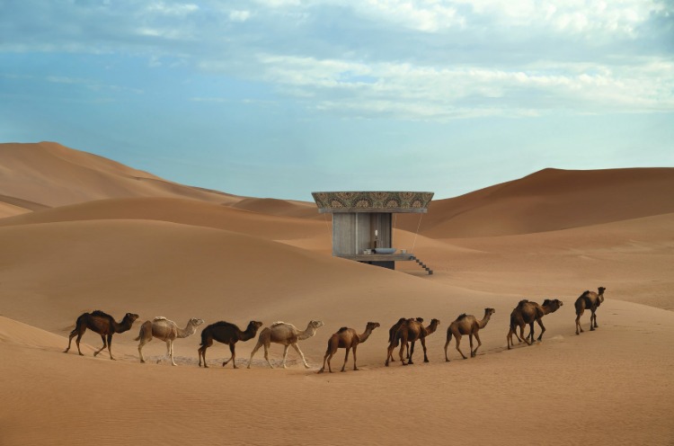 ett runt hus i öknen omgiven av kameler