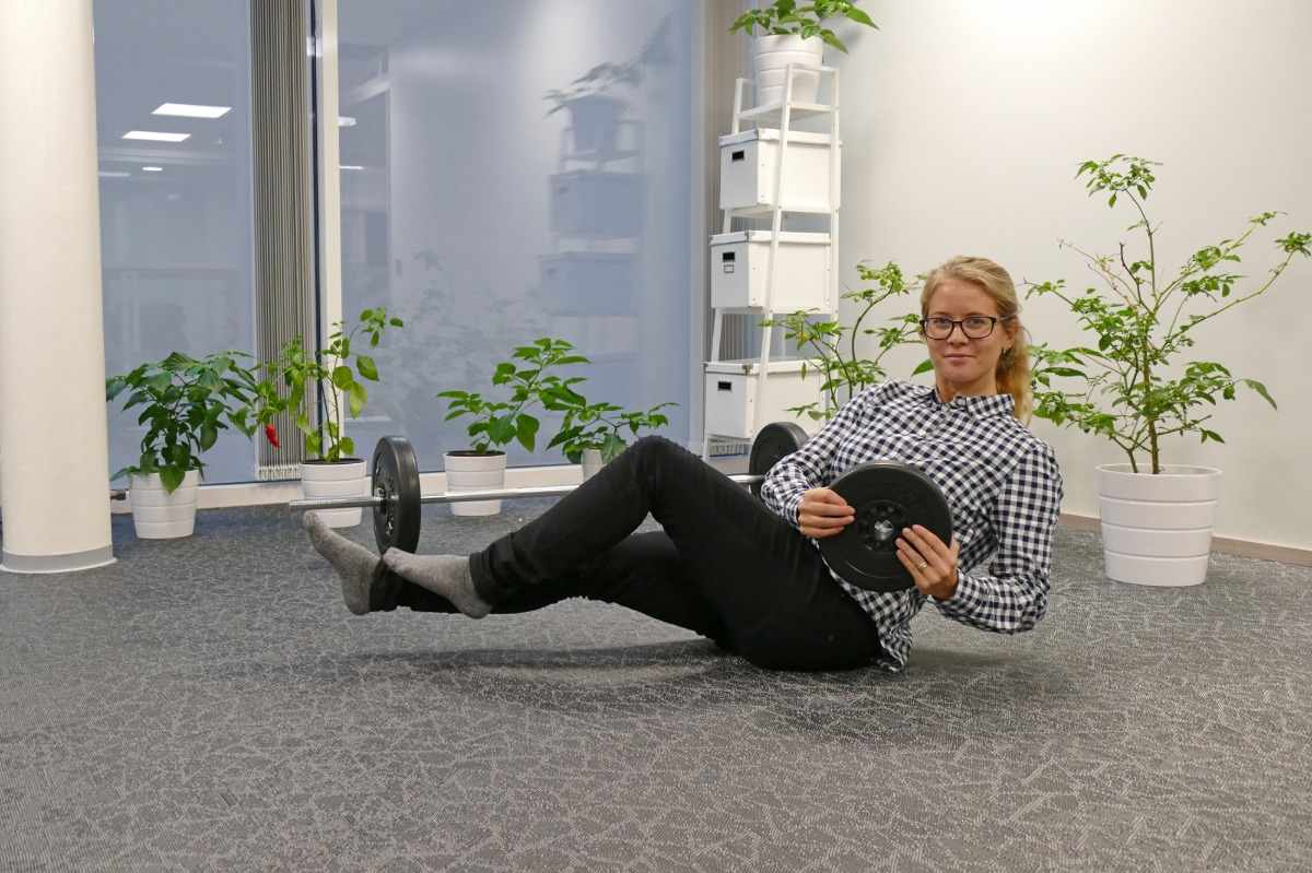 Blond kvinna på kontoret gör rysk twist -övning med vikten i händerna