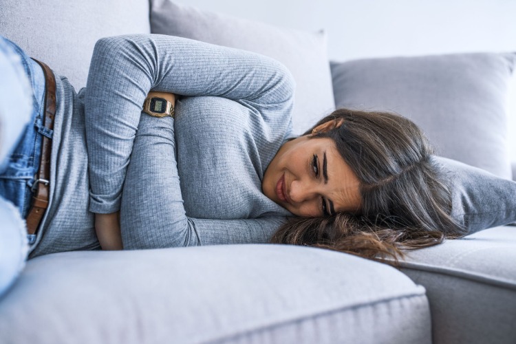 kvinna upplever salmonellasymtom som kräkningar och hög feber och ligger i soffan med magkramper