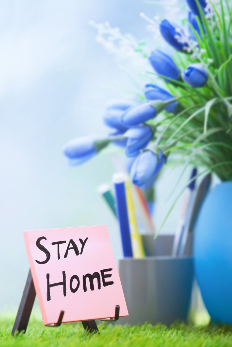 lapp med stanna hemma på grund av sars coronavirus skriver bredvid blå blommor i vas