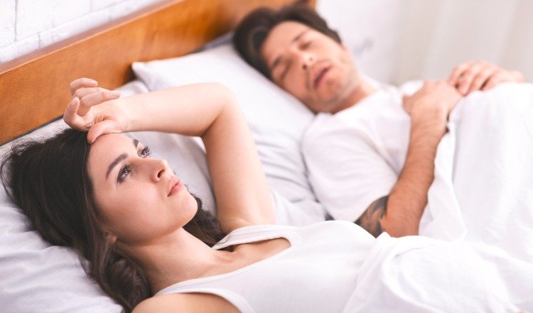 ung kvinna ligger sömnlös i sängen bredvid mannen