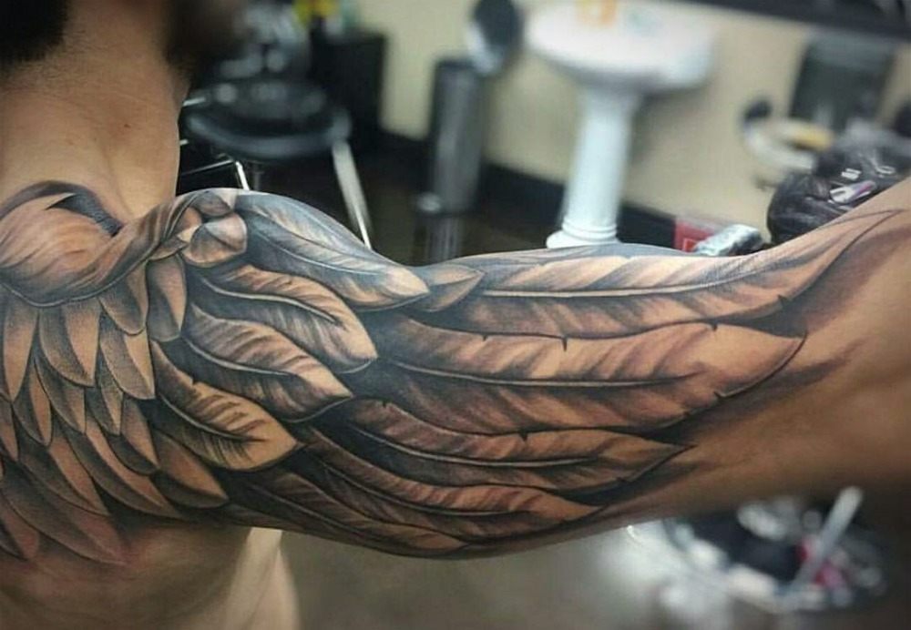 utsträckt arm med vingtatuering i svarta detaljer och textur axeltatuering män