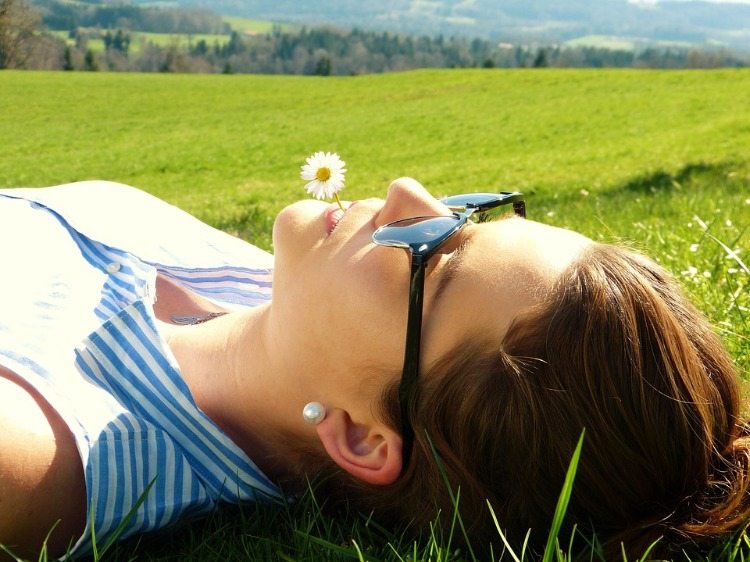 kvinna med solglasögon håller vit blomma i munnen under solstrålarna på en äng