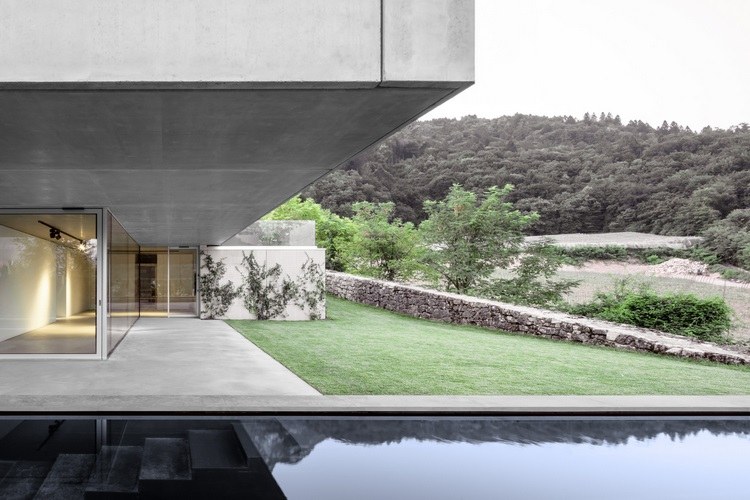 exponerat betonghus casa mf stora glasfönster modern minimalistisk design stenmur skog glidande glasdörr