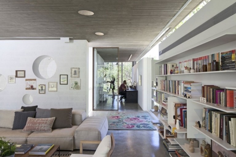 exponerad betong-interiör-vardagsrum-vägg-vit-vägg-hylla-böcker-soffa-moduler-kudde-matta