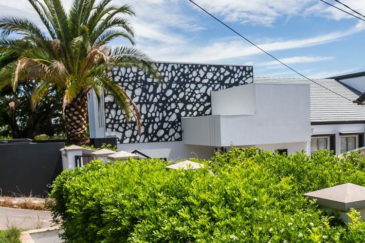 Sekretessstängsel-metall-fasad-svart-byggnad-vit-buske-palm-himmel