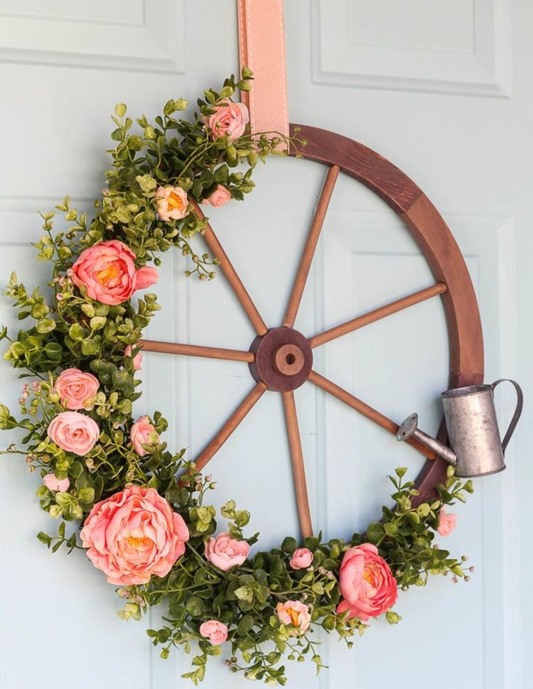 Original dörrkrans tillverkad av ett trähjul med rosor och en liten vattenkanna
