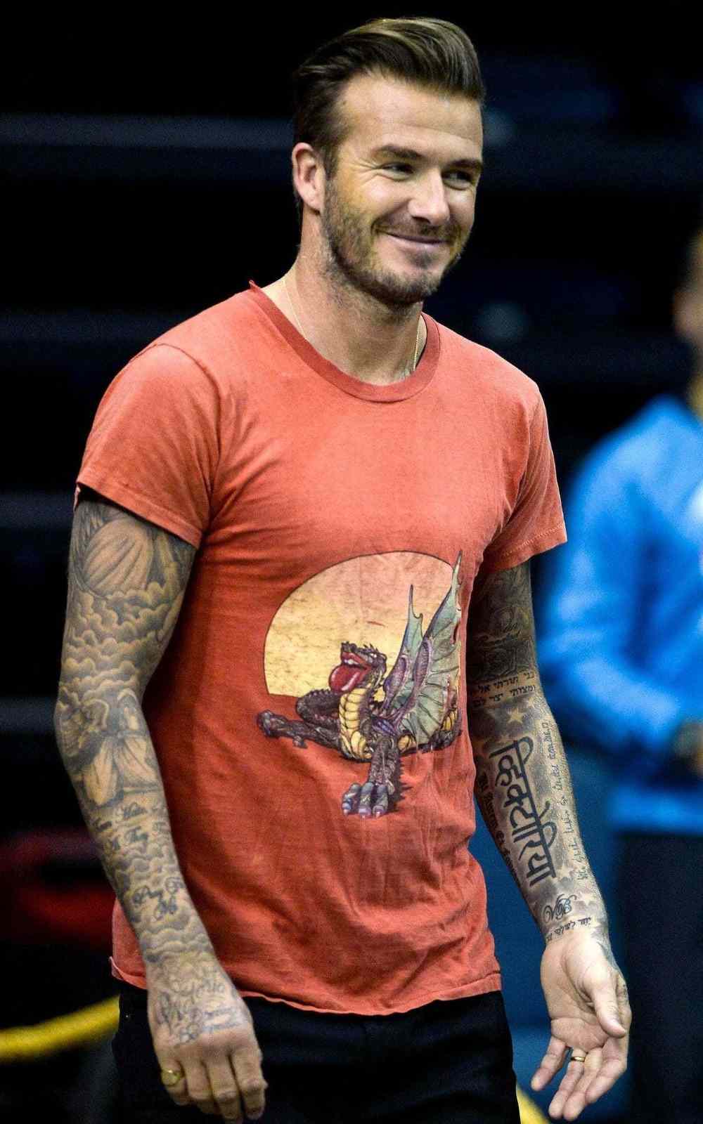 David Beckham med tatueringar på båda armarna och t-shirten ler