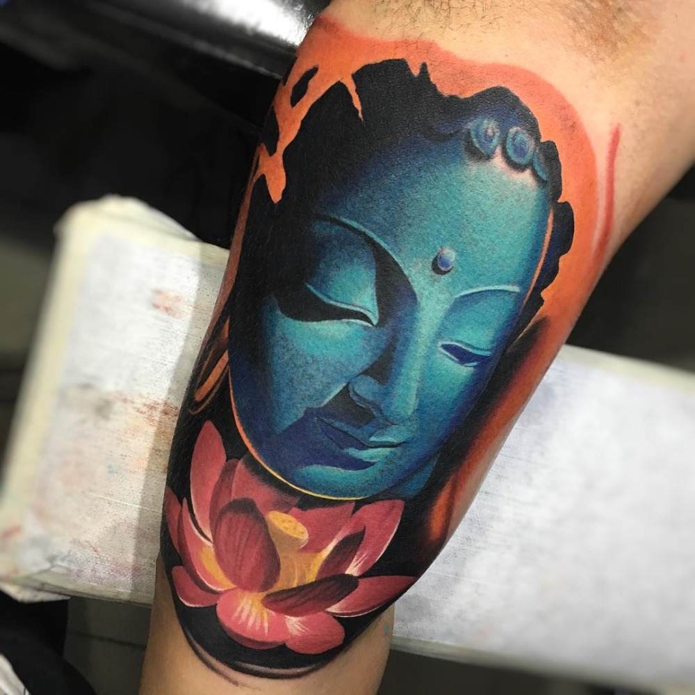 buddha tatuering överarm inuti färgad med blått och rött bläck lotusblomstatuering