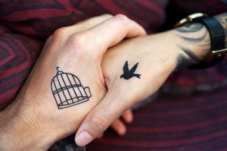 två händer som håller bur- och fågeltatueringar som symboler kombinerar och ansluter