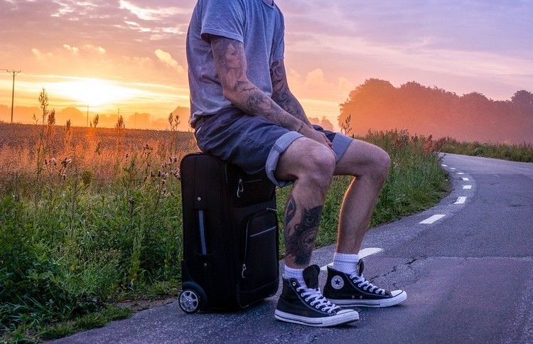 tatuerade mannen sitter på resväska bagage i solnedgången på vägen bredvid fältet