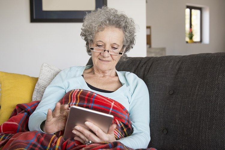 Äldre kvinna med grått hår läser e-böcker på e-läsare