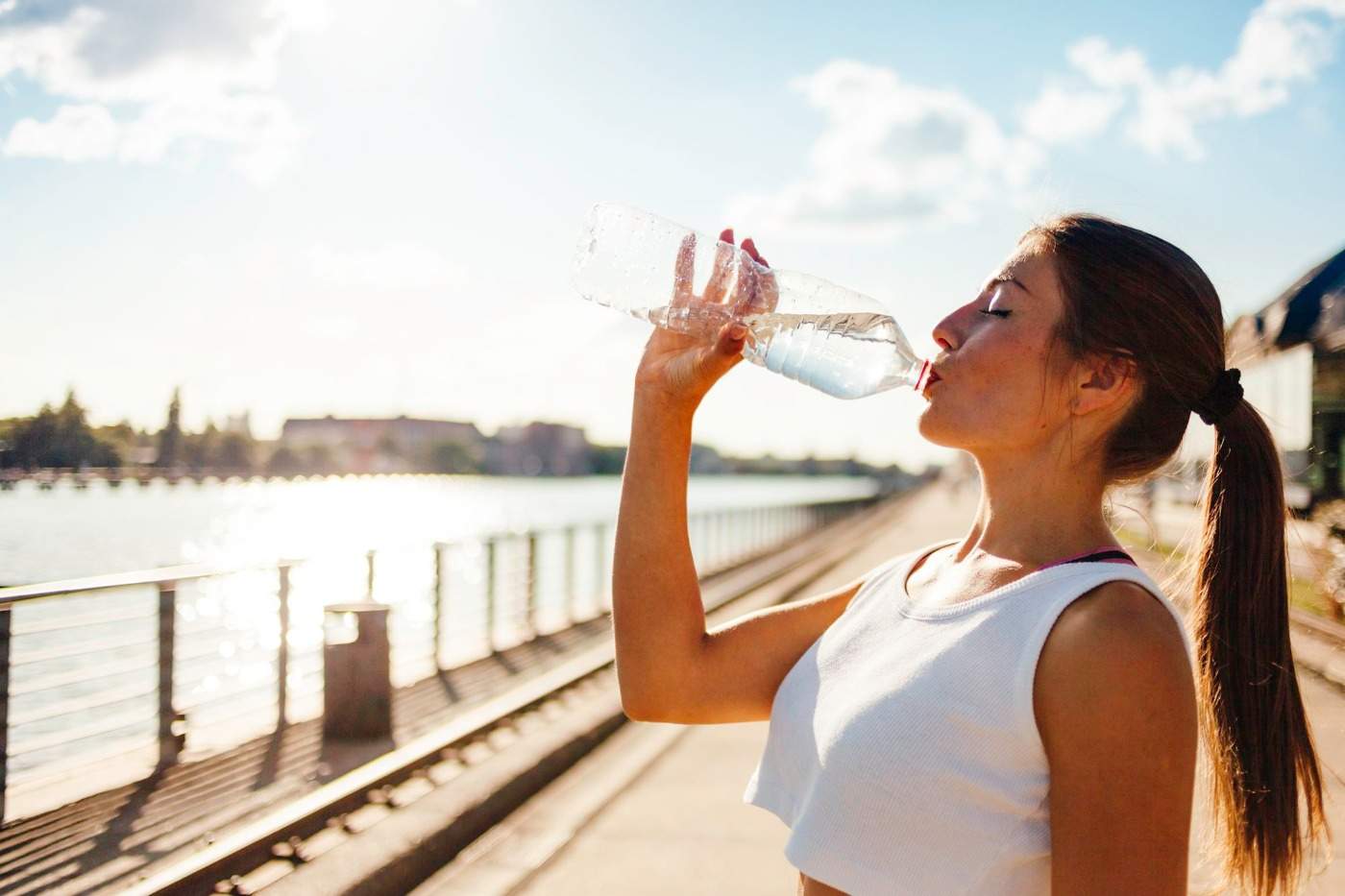kvinna som dricker vatten från plastflaska under solstrålarna bredvid en flod