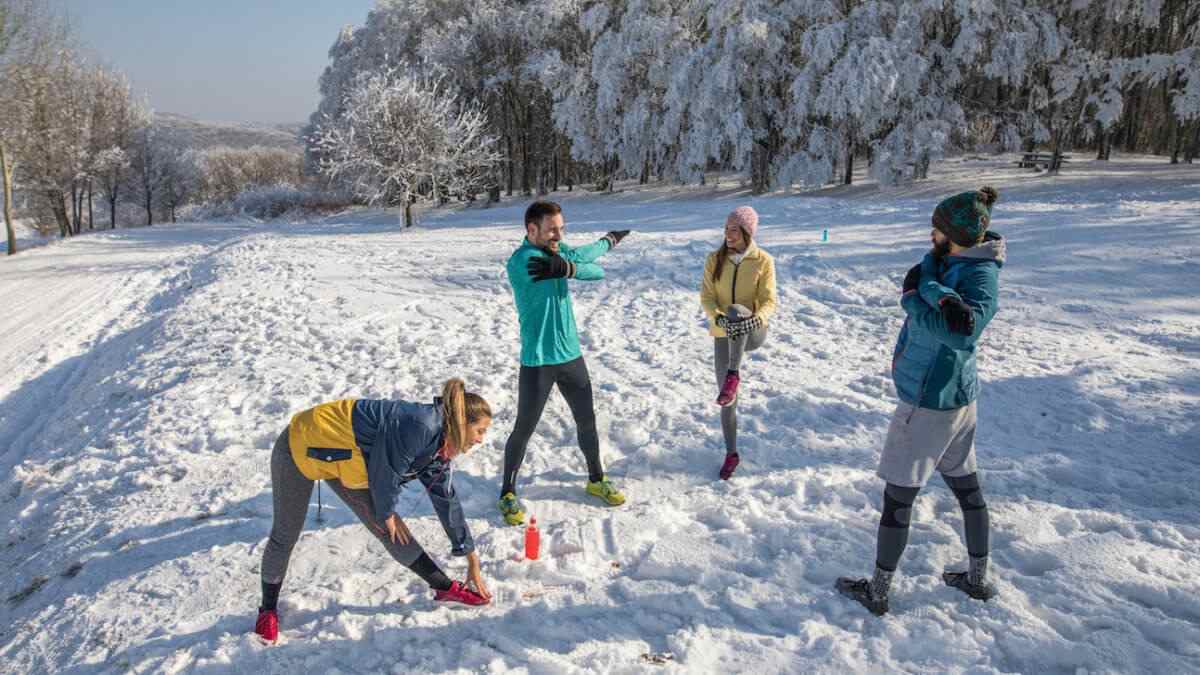 Grupp unga människor som sträcker sig i snön på vintersemester