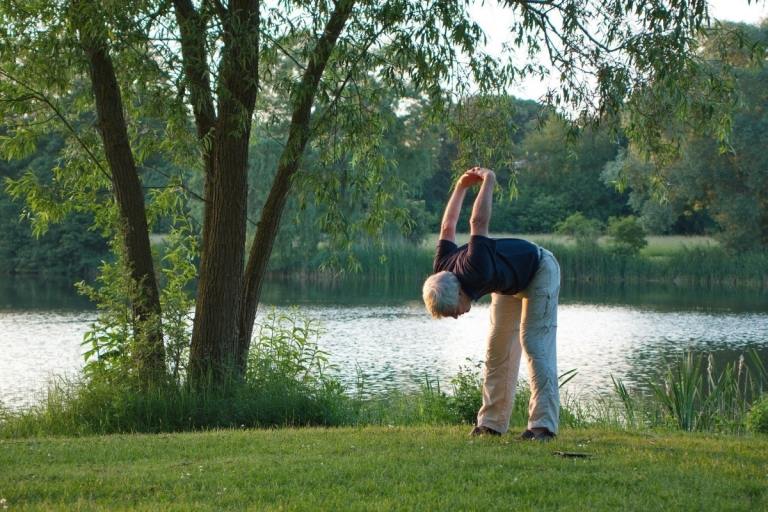 Äldre man gör yoga i naturen framför en sjö