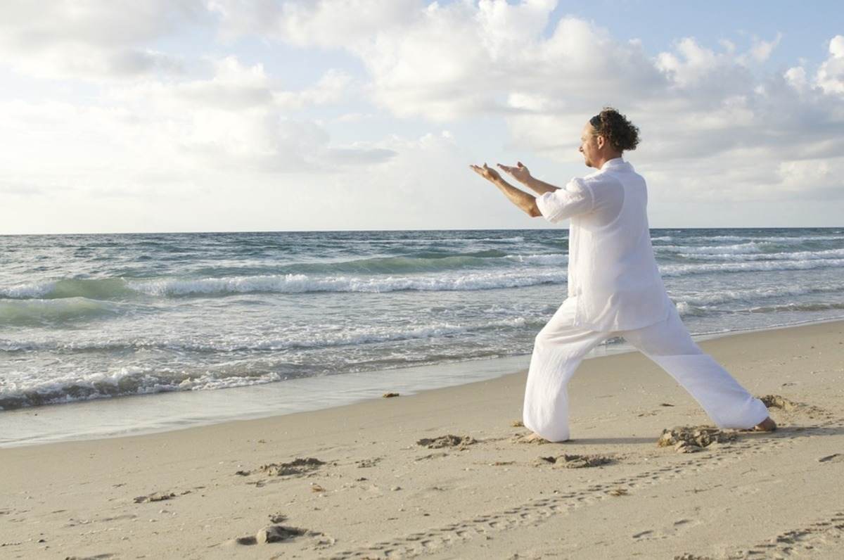 man i vita kläder som gör yoga på stranden