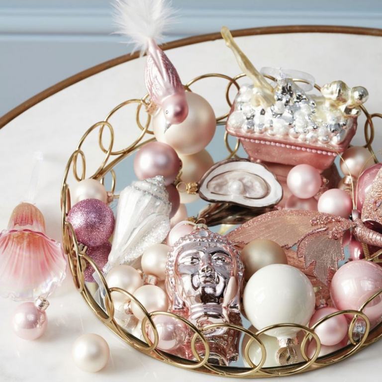 Vitt och dammigt rosa och roséguld julgransdekorationer arrangerade på ett guldfat