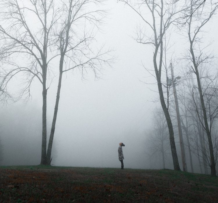 Kvinnan står ensam i parken höga träd och tjock dimma