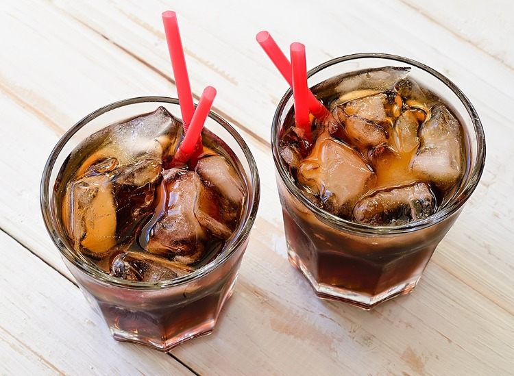 två glas kolsyrad dryck som cola och isbitar bredvid röda sugrör