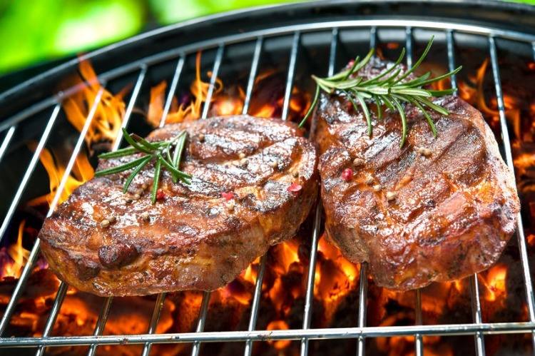 Grillade biffar med rosmarin på grill grillad med tända kol och lågor