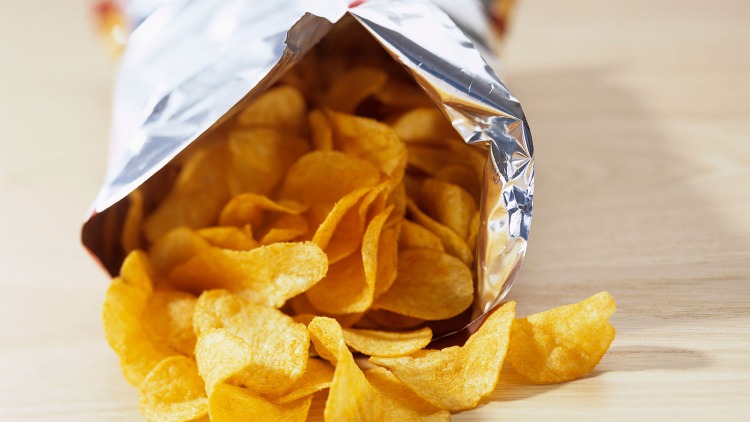 Potatischips från förpackningen fördelas på ett bord i närbild som en skadlig mat