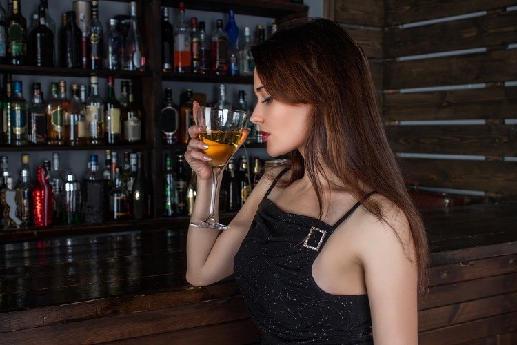 ung kvinna i en bar håller ett halvfullt vinglas framför andra alkoholflaskor