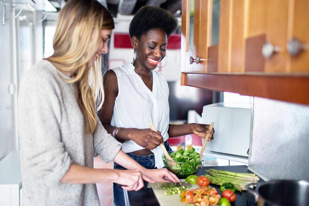 två kvinnor lagar och förbereder sallad med sparrisallat, vårlök och tomater