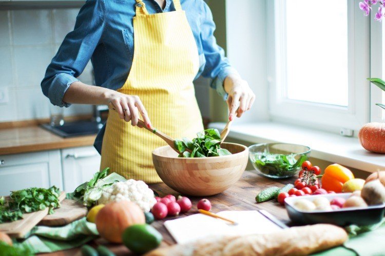 Kvinnan förbereder sallad i köket som består av spenatblad, rädisor, blomkålgurkor och andra grönsaker