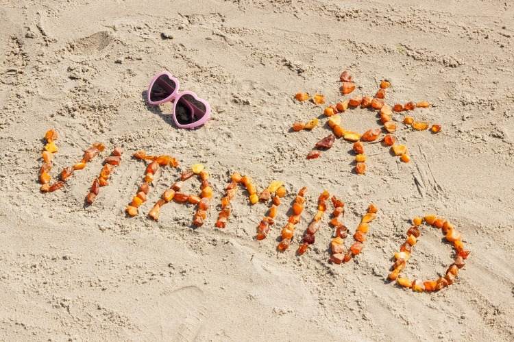 vitamin-d och solskrift inskriven med stenar på sanden
