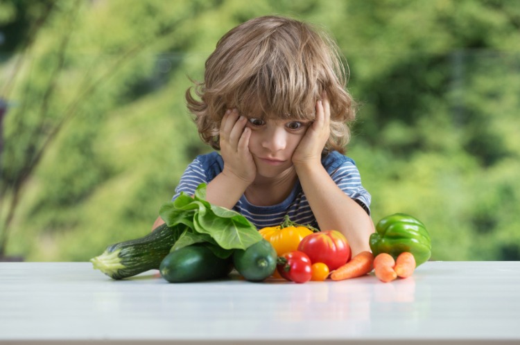 pojke tittar på grönsaker på bordet med skräck