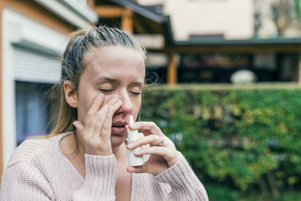 ung kvinna använder nässpray för hygien utomhus