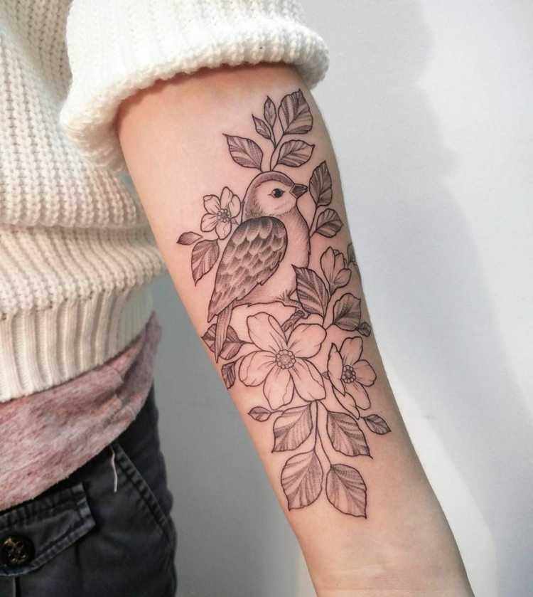 Damfågeltatuering med blommor på underarmen
