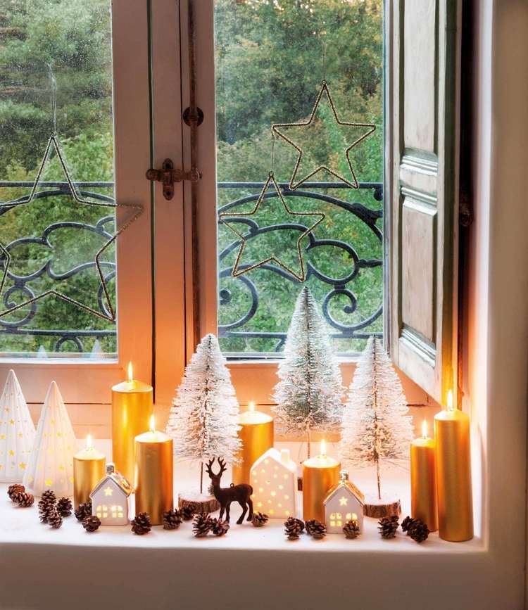Vinterdekoration till fönsterbrädan med gyllene pelarljuskottar och trädfigurer