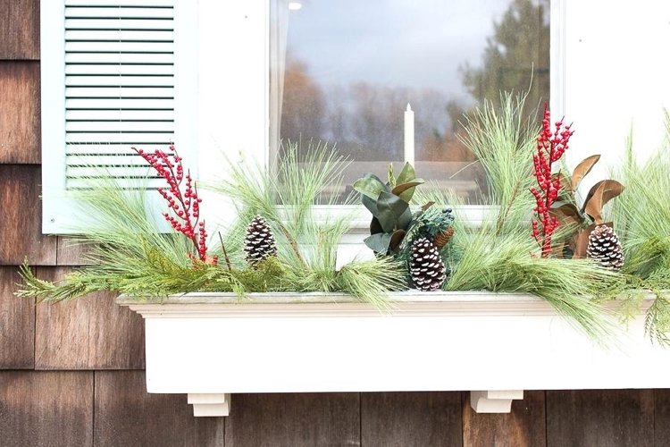 Juldekoration dekorerar puristiskt utsidan av fönsterbrädan med LED -ljus och nypon- och tallgrenar och kottar med konstsnö